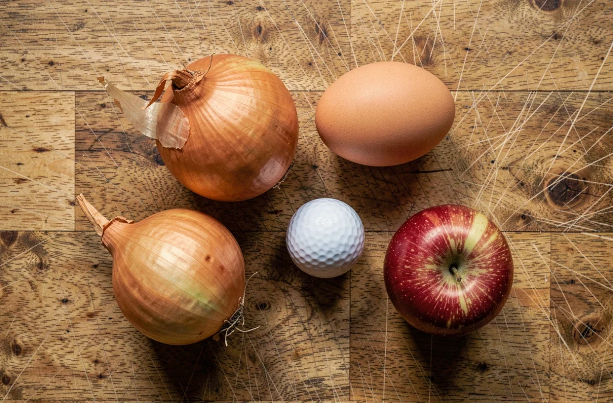 Vue de dessus d'oignons de différentes tailles comparés à des objets du quotidien pour estimer le poids sans balance